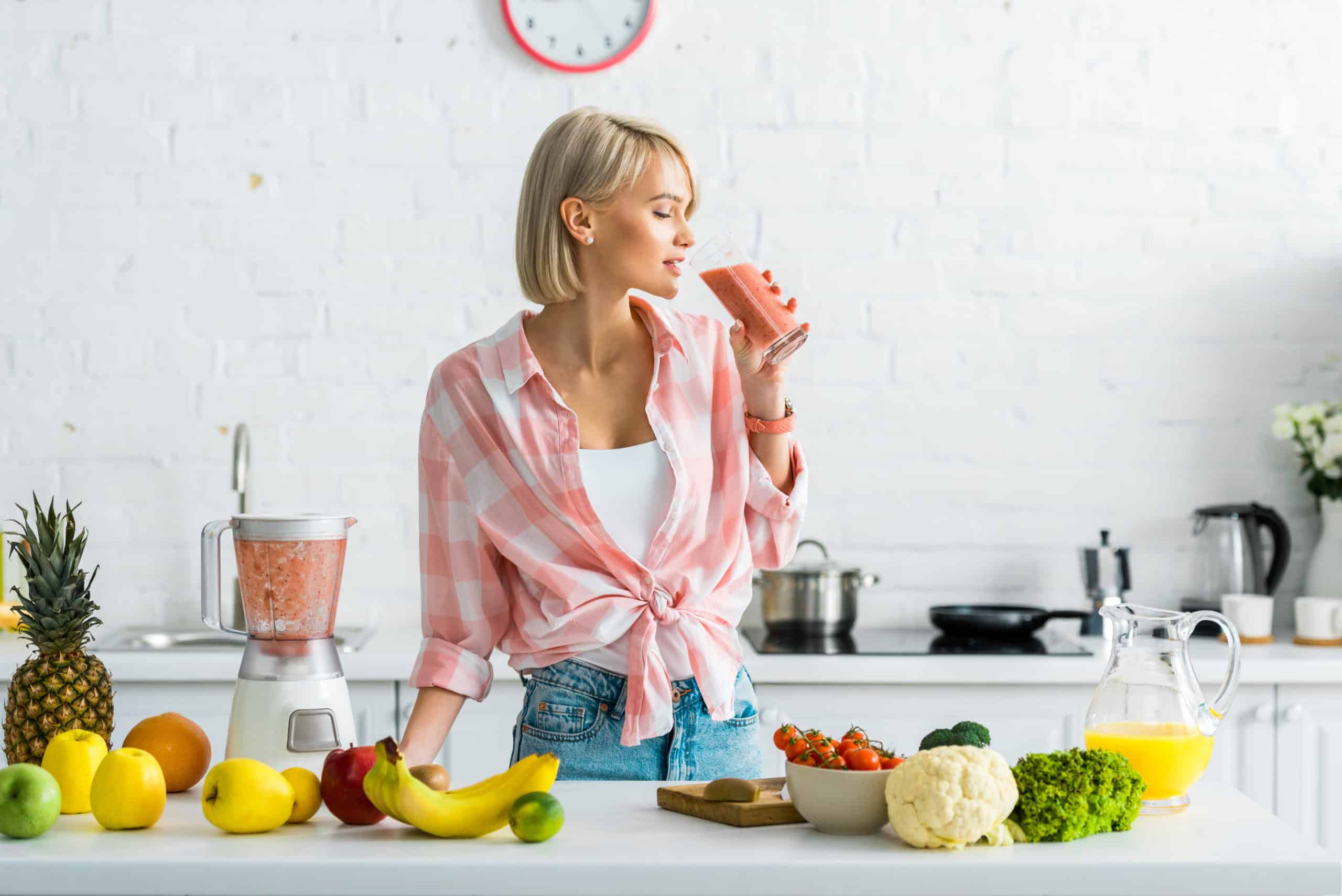 attractive blonde woman drinking tasty smoothie near ingredients in kitchen